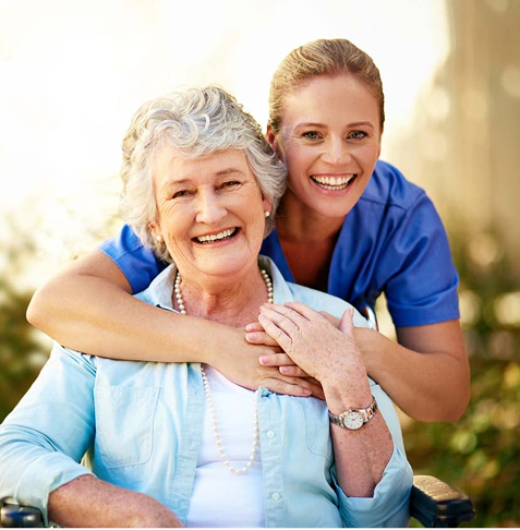 A caregiver warmly embraces an elderly woman outdoors.
