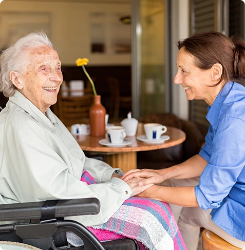 Senior lady with her caregiver, smiling in a dining setup.